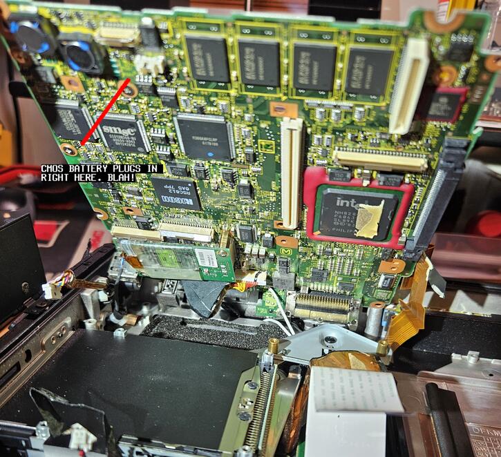 A close-up shot of the bottom of the lifted motherboard showing where the CMOS battery plugs in