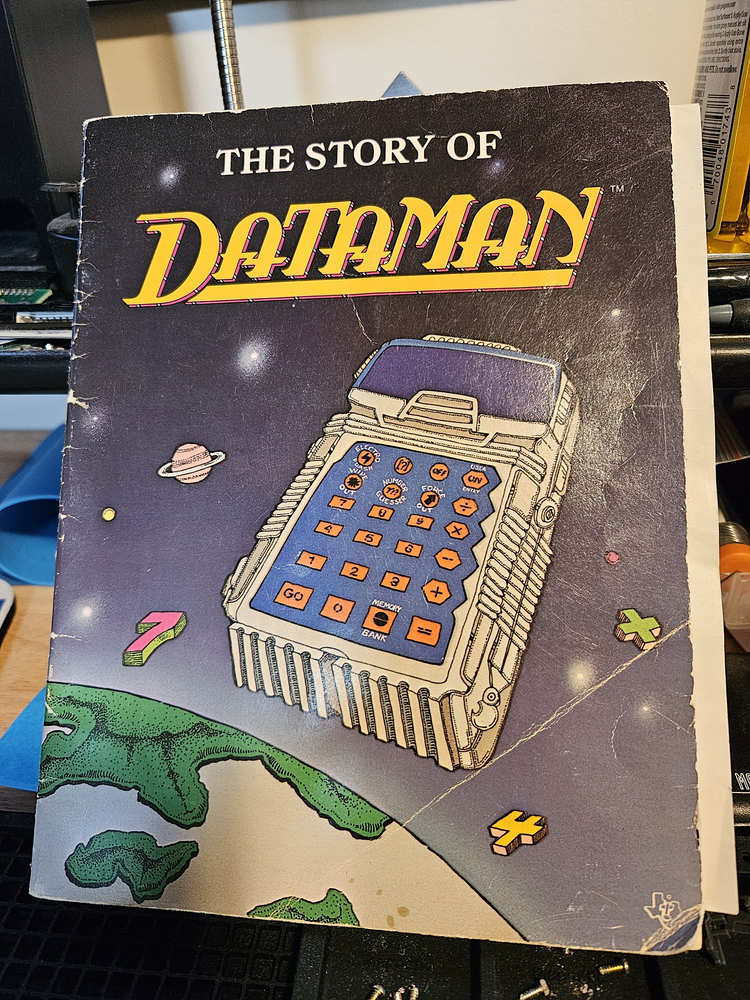 pictured is the front cover the DataMan manual, entitled 'The Story of DataMan', featuring the boxy toy calculator orbiting over the Earth like some kind of space coffin for the dead concept of fun math